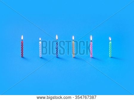 Congratulation composition from burning verticaly standing candles for sweet cakes on a blue background with copy space. Birthday party composition.