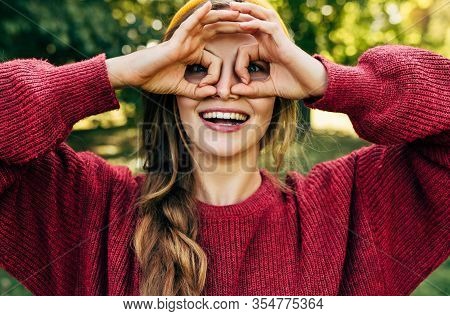 Beautiful Woman Wearing A Red Sweater Doing Ok Gesture Like Binoculars, Smiling Broadly And Looking 
