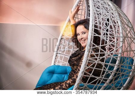 Fat Plump Charming Cute Woman With Black Curly Hair In Black Beautiful Dress In A White Wicker Chair