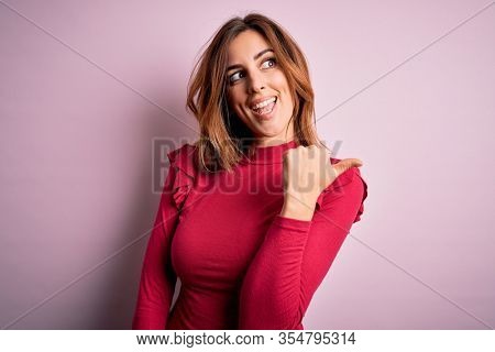 Young beautiful brunette woman wearing casual sweater stnding over pink background smiling with happy face looking and pointing to the side with thumb up.