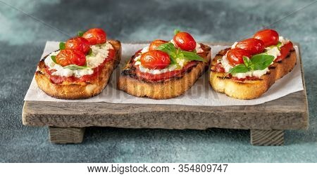 Italian Bruschettas With Mozzarella, Riccotta, Baked Tomatoes And Basil