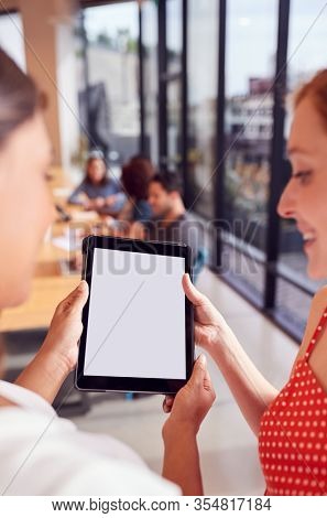 Close Up Of Two Businesswomen Looking At Digital Tablet In Shared Office Workspace