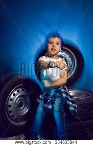 Boy In A White T Shirt Shirt And Hat Sits On A Background Of Car Wheels
