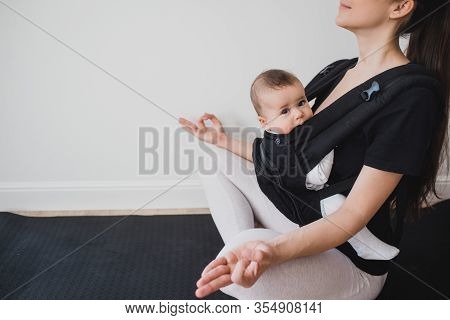 Young Mother Doing Yoga Exercises And Meditation With Her Little Baby In Ergo Backpack.
