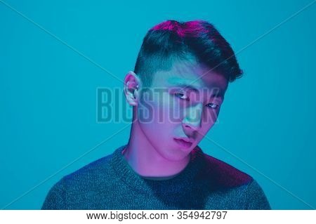 Portrait Of A Guy With Colorful Neon Light On Blue Studio Background. Male Model With Calm And Serio