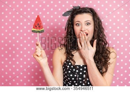 Astounded Young Dirl Is Covering Her Mouth By Hand, Her Eyes Widely Opened, Watermelon Lollipop In H