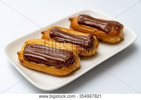 Plate Custard Cakes With Chocolate Icing On A White Background. Copy Space