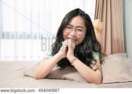 Beautiful Asian Woman Hold Her Hands Together While Lie On Her Stomach On Bed In Bedroom With A Past