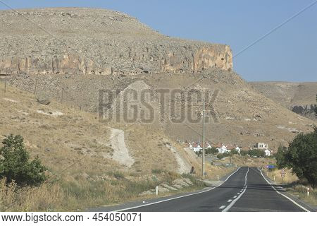 Desert Highway And Ancient Dwellings In Caves In The Rocks At Sunset On Kayseri Province, Turkey, As
