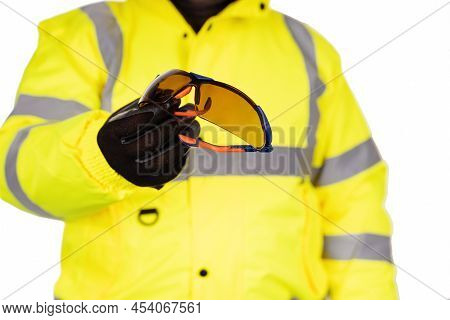 A Construction Worker In A Yellow Hi-viz Coat On A White Background Gives Dark Tinted Safety Glasses