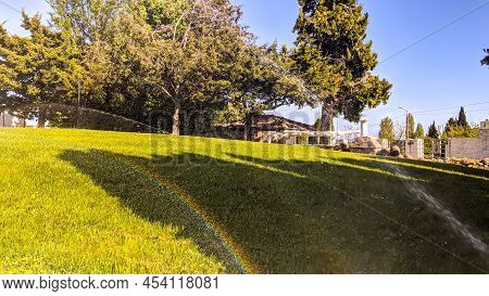 A Bright, Beautiful, Colorful Rainbow Against The Backdrop Of A Green Flowering Lawn With Freshly Cu