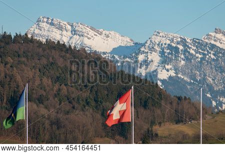 Wangen-lachen, Switzerland, February 13, 2022 Waving Swiss Flag With The Snow Covered Alps In The Ba