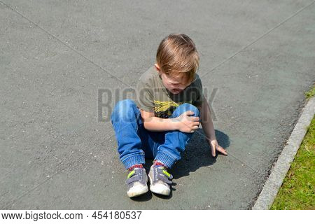 A Crying Boy On The Floor In Pain And Holding His Knee. High Quality Photo