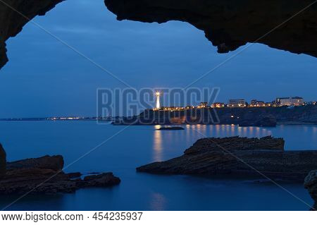 The Night View Of The Biarritz Lighthouse Seen Through Rock Arch . France.