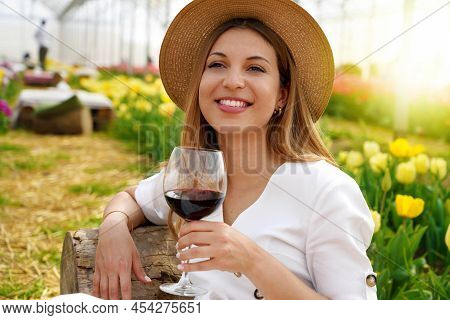 Relaxed Beautiful Woman Enjoying A Glass Of Red Wine Between Tulips On Spring Time
