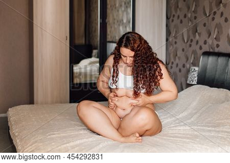 Curly Plus Size Woman In White Underwear Sitting On Bed In Bedroom And Pinch Sagging Folds On Thick 