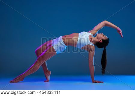 Portrait Of Young Soprtive Woman Training Isolated Over Blue Studio Background In Neon Light. Stretc