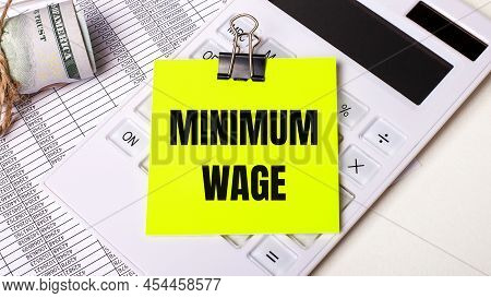 On A Light Background - Cash, A White Calculator And A Yellow Sticker Under A Black Paper Clip With 