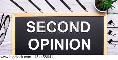 On A Light Wooden Table - A Board With The Text Second Opinion, Pencils, Plants, Glasses And Paper C