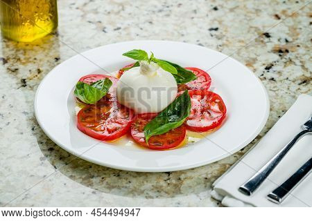 Salad With Buratta Cheese And Tomatoes With Basil On White Plate On Marble Table