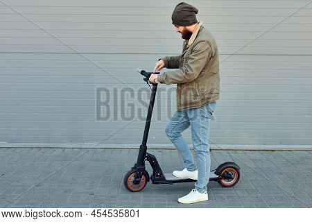 The Man With Electric Scooter Near Wall. Ecological Transportation Concept. Stylish Bearded Male Usi