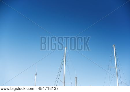 Upper Section Of Sea Yachts Against The Blue Sky. White Masts Of Sea Yachts, Standing At The Pier In