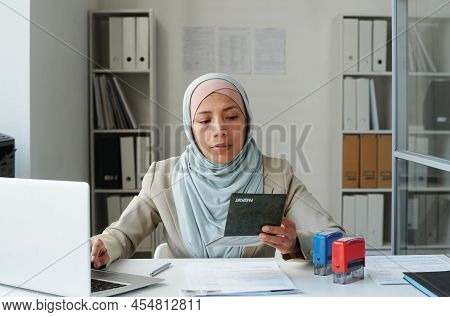 Modern Muslim Woman Working In Embassy Office Adding Passport Information About Citizen Into Compute