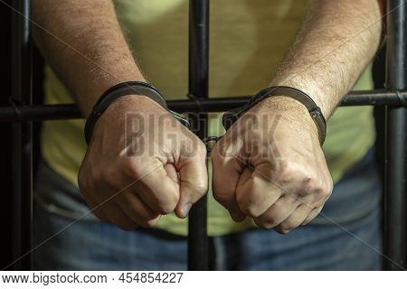 A Man In Handcuffs In A Cell Behind Bars. Concept: A Prisoner In A Courtroom, A Court Sentence To A 