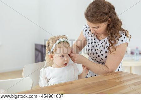 Mother Helps To Put On Cochlear Implant For Her Deaf Little Daughter. Hearing Aid And Deafness Conce