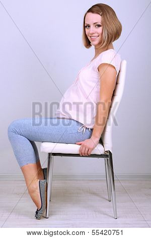 Young regnant woman sitting on chair on wall background