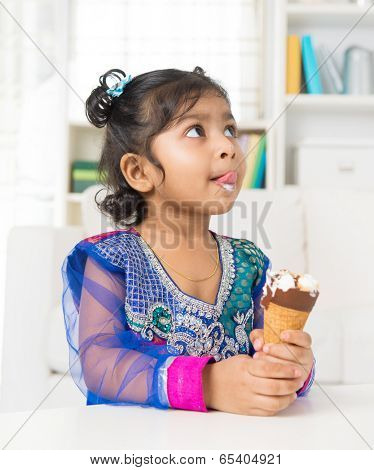 Little Indian girl licking her lips with an ice cream cone in hand, family living lifestyle at home.