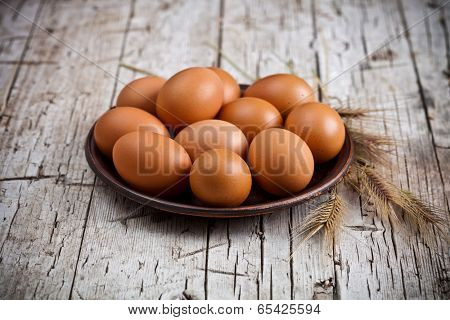  fresh brown eggs in plate and wheat ears on rustic wooden background
