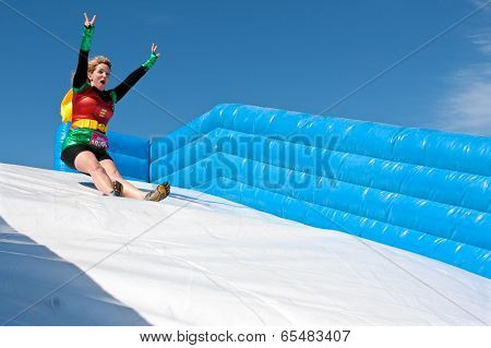 Woman Wearing Superhero Costume Goes Down Obstacle Race Slide