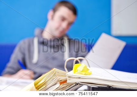 Realistic image of Paperwork, with a folder, filled with documents on a desk, with a young man behind it, reading from a heet of paper, and taking notes