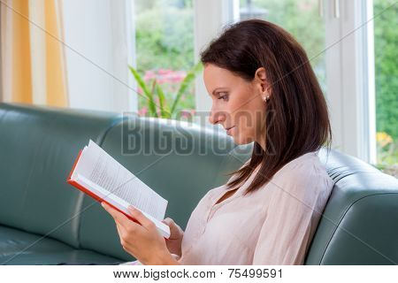 a young woman sitting on a couch and reading a book