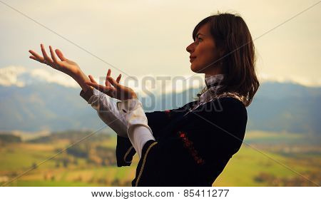 beautiful young woman with dark hair and a historical dress posing on a meadow in open lanscape wit