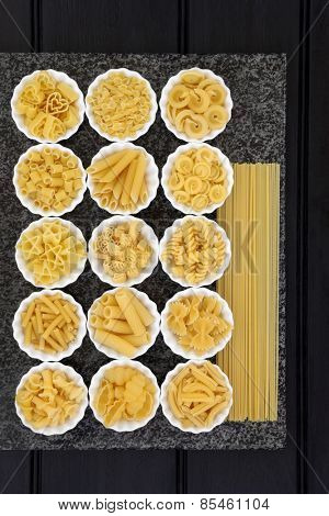 Pasta spaghetti dried food selection in porcelain crinkle bowls on a marble slab over dark wood  background.