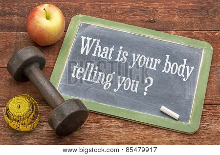 What is your body telling you?  A question on a slate blackboard against weathered red painted barn wood with a dumbbell, apple and tape measure