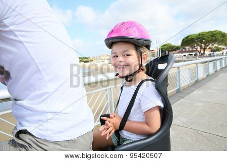 Smiling little girl sitting in child seat on bicycle