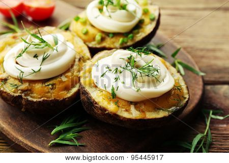 Baked potato with mayonnaise and herbs on wooden cutting board, closeup