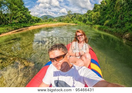Young couple making a selfie shot while canoeing in Kao Sok rainforest river