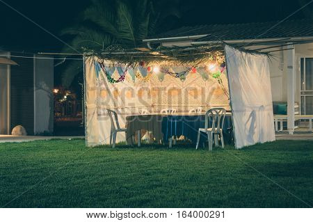 Fabric sukkah decorated with printed pattern and hebrew text of blessing: Grant peace everywhere goodness and blessing Grace lovingkindness and mercy to us and unto all Israel Your people. Night toned image