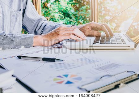 Business man hand working with business graph or analysis chart and using laptop computer .Close up business team analysis and strategy concept with sun flare.