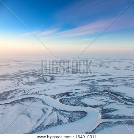 Aerial view above the endless snow covered tundra river in time of short winter day.