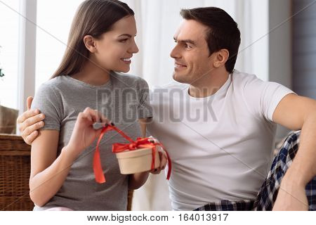 Time to open presents. Happy pretty young woman opening her present and smiling while looking at his boyfriend