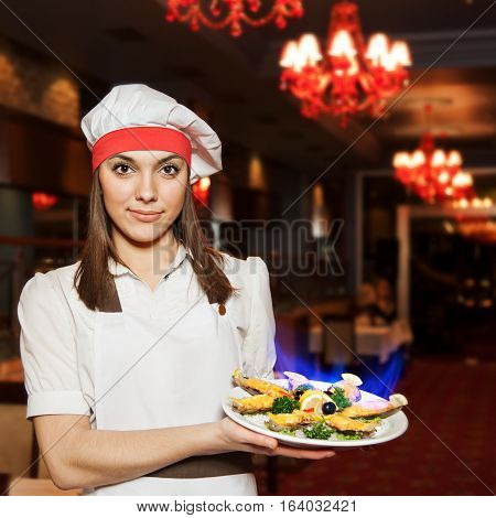 Young attractive female chef with dishes of mussels with fire