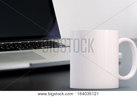 Mockup Styled Stock Product Image white mug that you can add your custom design/quote to. Mug is in front of an open laptop.