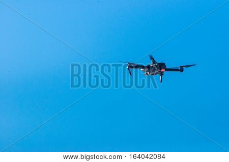 Small grey modern drone hovering against blue sky