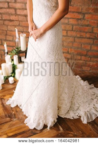 the beautiful bride in a white guipure elegant dress. the bride against the background of a brick wall and candles.