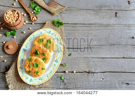 Fried pea patties on a plate. Healthy diet patties cooked from yellow dried peas and decorated with parsley. Small barrel with dried peas on old wooden background with copy space. Vegetarian food
